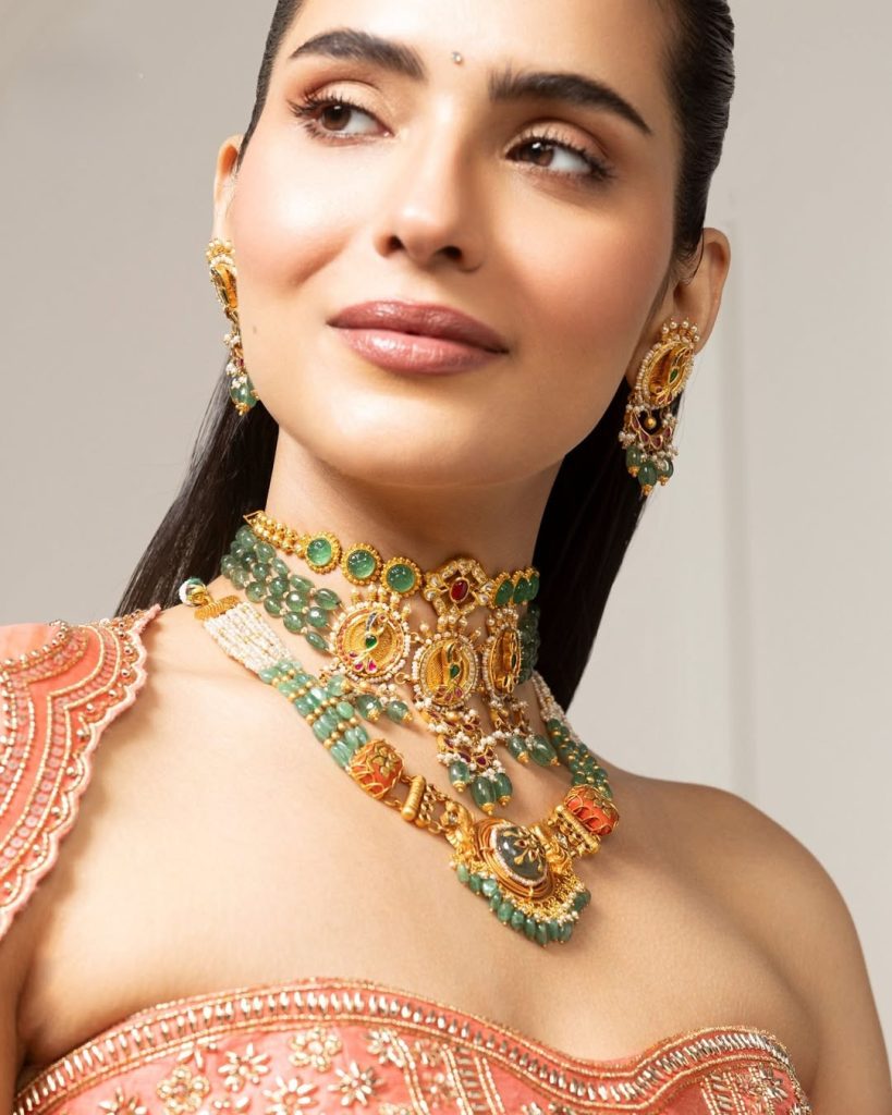 Bride in coral embroidered outfit wearing layered gold choker with green stone accents 