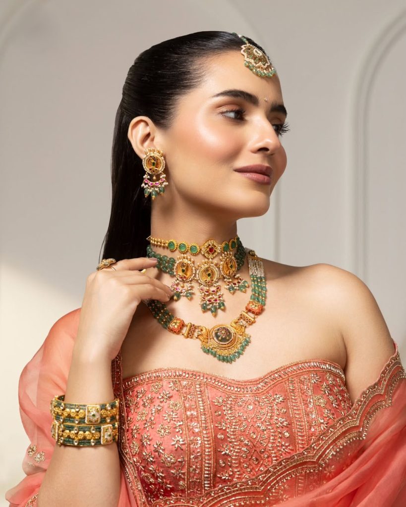 Bride in coral embroidered outfit wearing layered gold choker with green stone accents 