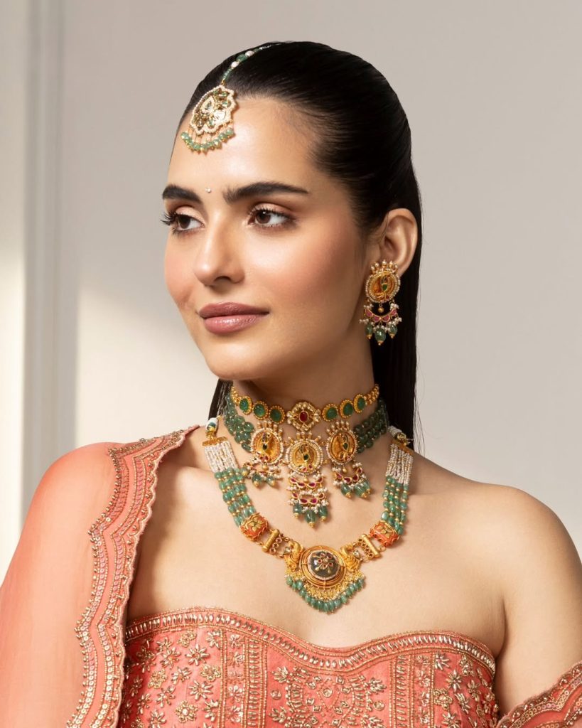 Bride in coral embroidered outfit wearing layered gold choker with green stone accents 