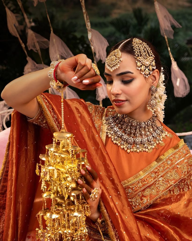 Bride in orange ensemble wearing heavy polki choker with layered pearl drops and matha patti. 