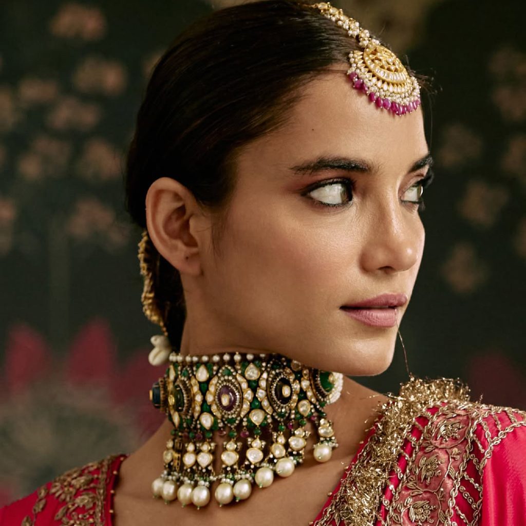 Bride in red ensemble wearing kundan polki choker with emerald and pearl drops. 