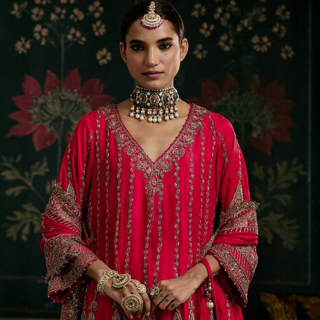 Bride in red ensemble wearing kundan polki choker with emerald and pearl drops. 