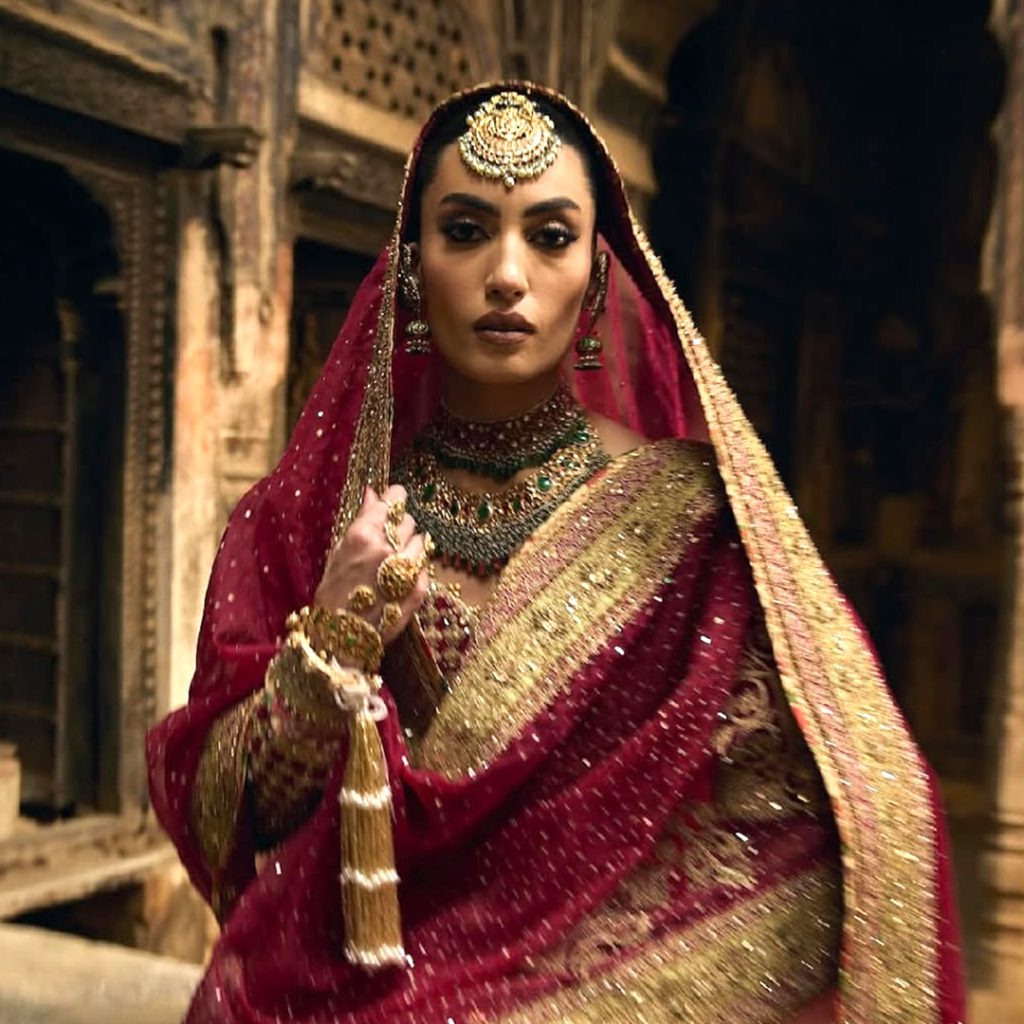 Bride in red lehenga wearing layered polki bridal necklace with emerald drops. 