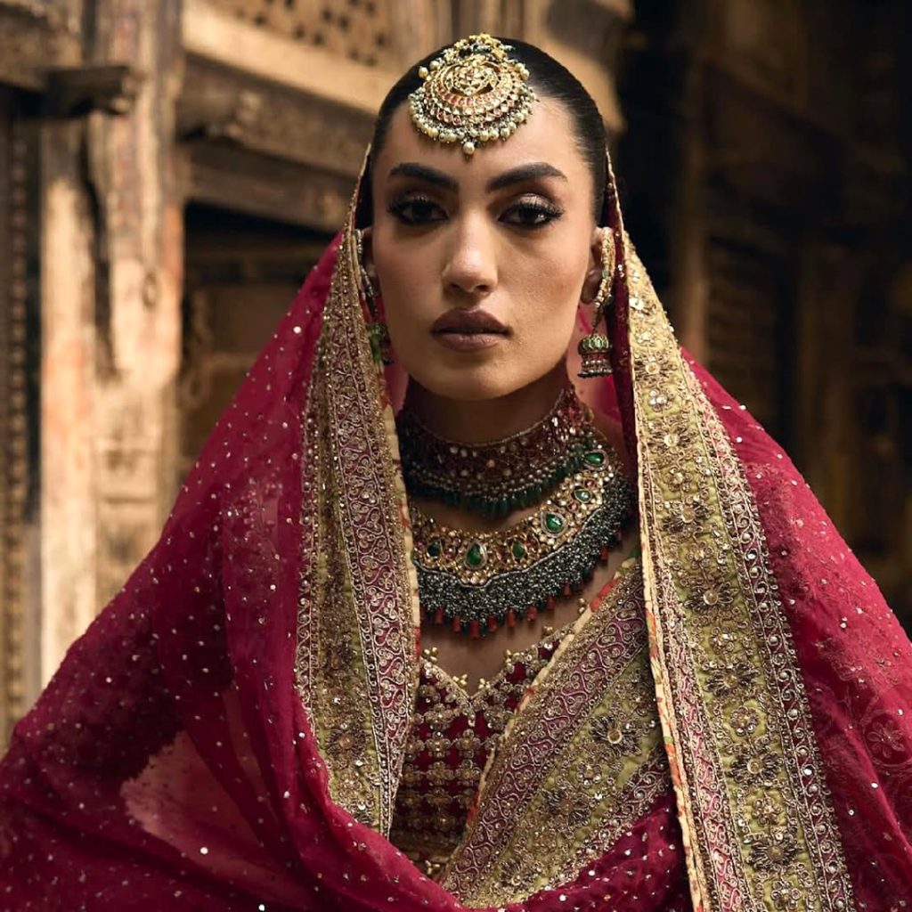 Bride in red lehenga wearing layered polki bridal necklace with emerald drops. 