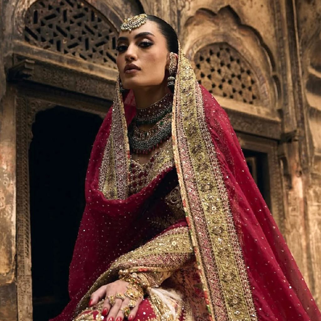 Bride in red lehenga wearing layered polki bridal necklace with emerald drops. 