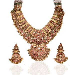 Heavy layered gold necklace by MJR Jewels with pink kundan stones, crescent motifs and pearl strands displayed on textured backdrop