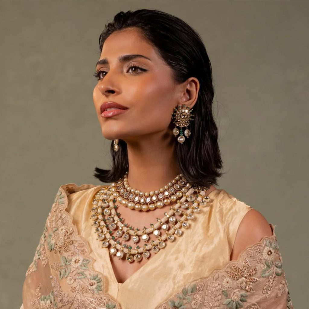 Model in beige embroidered outfit wearing layered uncut diamond and pearl necklace. 