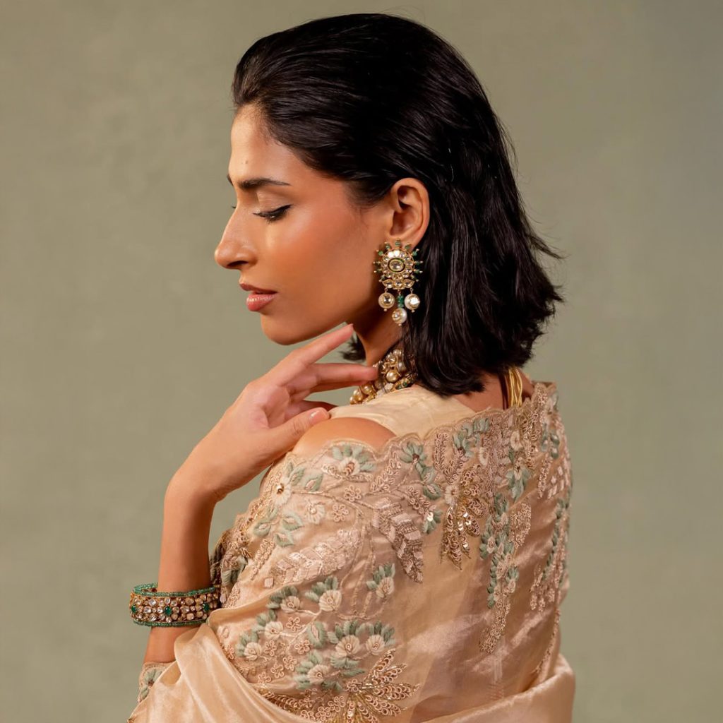 Model in beige embroidered outfit wearing layered uncut diamond and pearl necklace. 