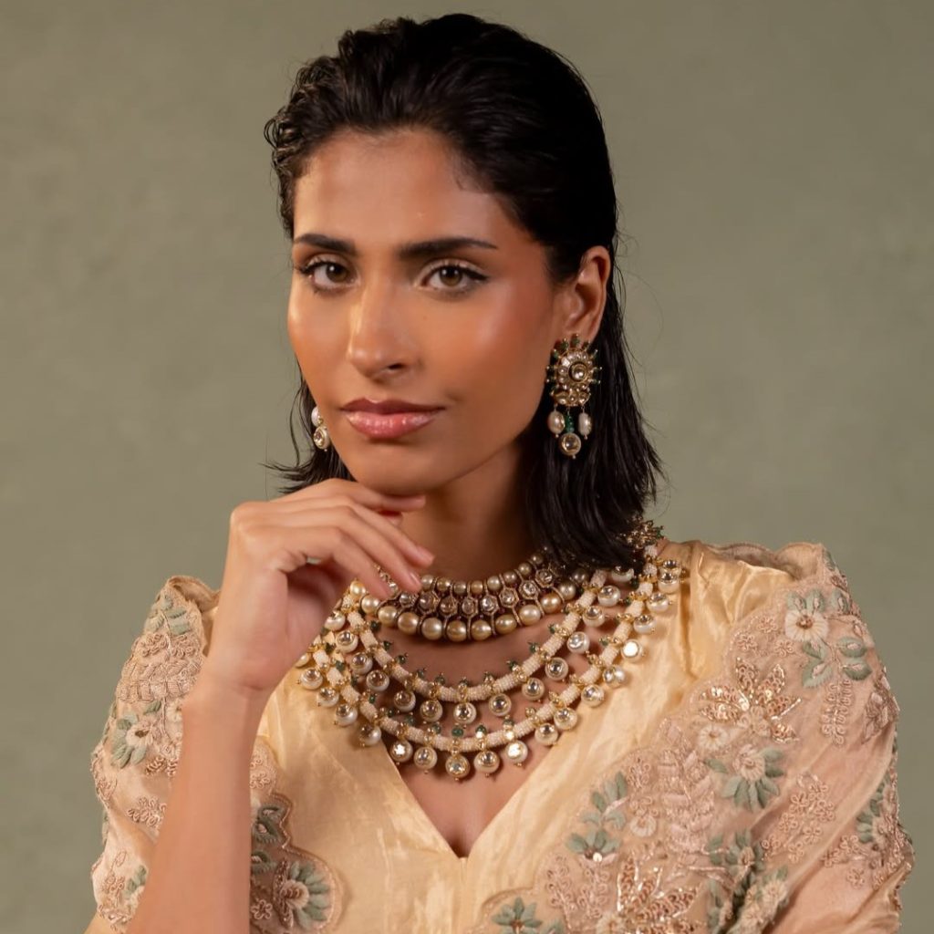 Model in beige embroidered outfit wearing layered uncut diamond and pearl necklace. 