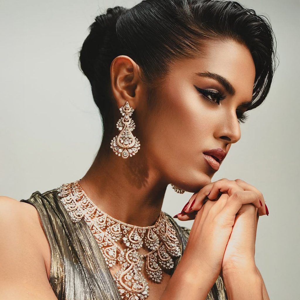 Model in metallic gown wearing intricate diamond choker and statement earrings. 