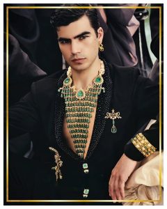 Male model in black outfit wearing dramatic layered emerald and gold statement necklace by Raabta by Rahul.