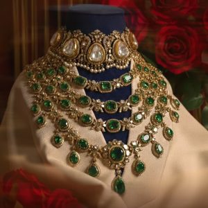 Layered emerald and polki necklace with gold detailing by Raniwala 1881 displayed on a mannequin with red roses in the background.