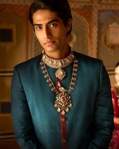Male groom in teal sherwani wearing layered polki and gemstone necklaces by Raniwala 1881.