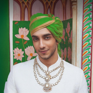 Vedang Raina wearing layered heritage necklaces with a green turban and ivory sherwani featuring jewellery by Raniwala 1881.