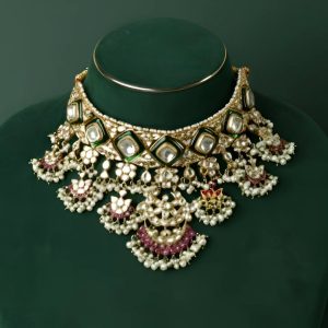 Traditional polki and kundan choker with green enamel and pearl drops by Saheli Jewellers displayed on a deep green bust.