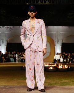 Male runway model in embroidered striped suit wearing a bold diamond statement necklace.
