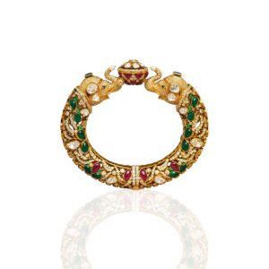 Gold kada with elephant head motifs, polki diamonds and green stones by Shubham Motiwala & Jewellers on a soft pastel background.