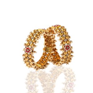 Pair of gold bangles with large gold beads and pearl embellishments by Sumeet Jewellers on a white background.