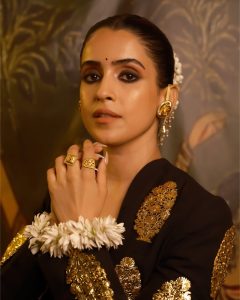 Sanya Malhotra wearing traditional gold rings and ear jewellery by Manubhai Jewellers styled with a dark festive outfit.
