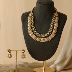 Gold and polki layered necklace with matching earrings by Tulsyan Jewellers displayed on a black mannequin with beige draped background.