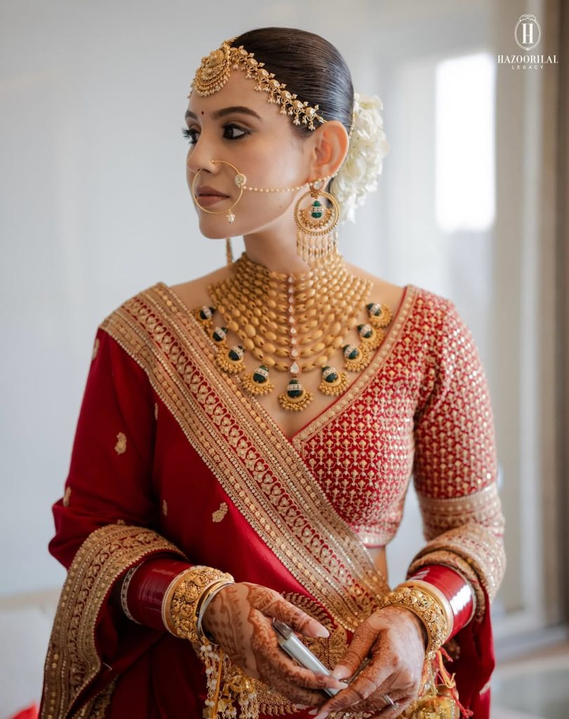 Bride in red outfit wearing structured gold choker with green stone drops and statement earrings