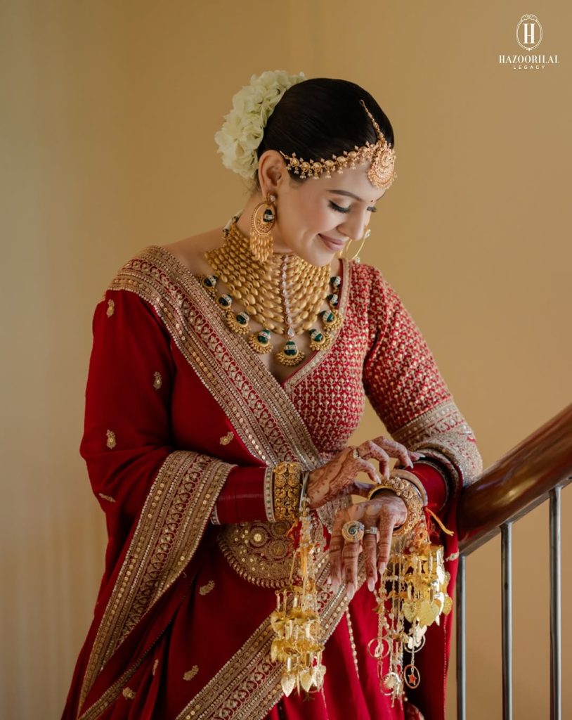 Bride in red outfit wearing structured gold choker with green stone drops and statement earrings
