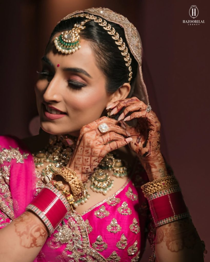 Bride in pink lehenga styled with layered polki choker necklace with green bead drops and matching earrings