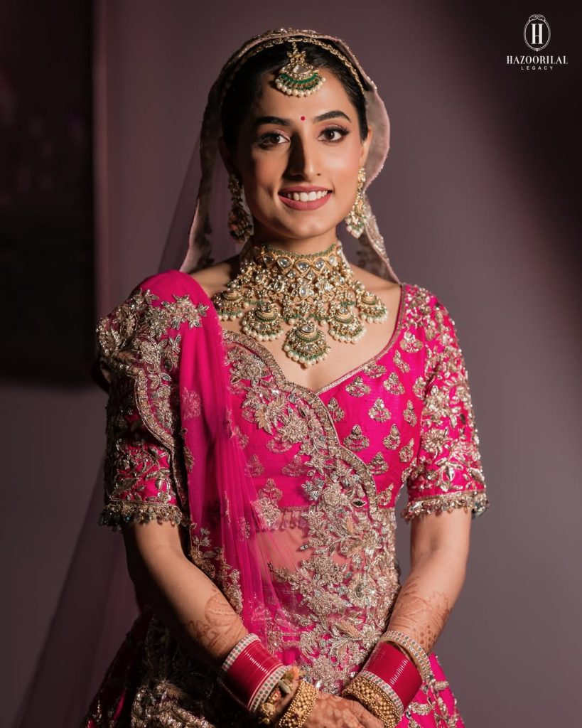 Bride in pink lehenga styled with layered polki choker necklace with green bead drops and matching earrings
