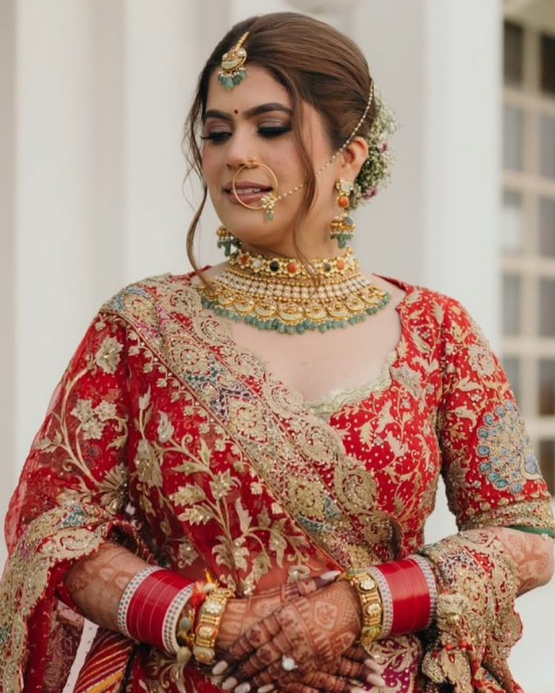 Bride in red lehenga wearing gold choker with navratna-inspired coloured stones and traditional bangles