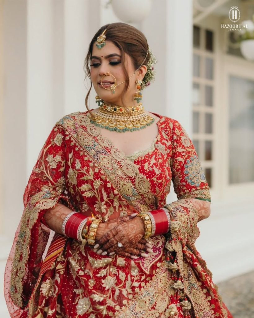 Bride in red lehenga wearing gold choker with navratna-inspired coloured stones and traditional bangles