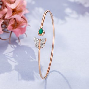 Gold open bangle with diamond butterfly and green stone detail by Akshaya Gold & Diamonds
