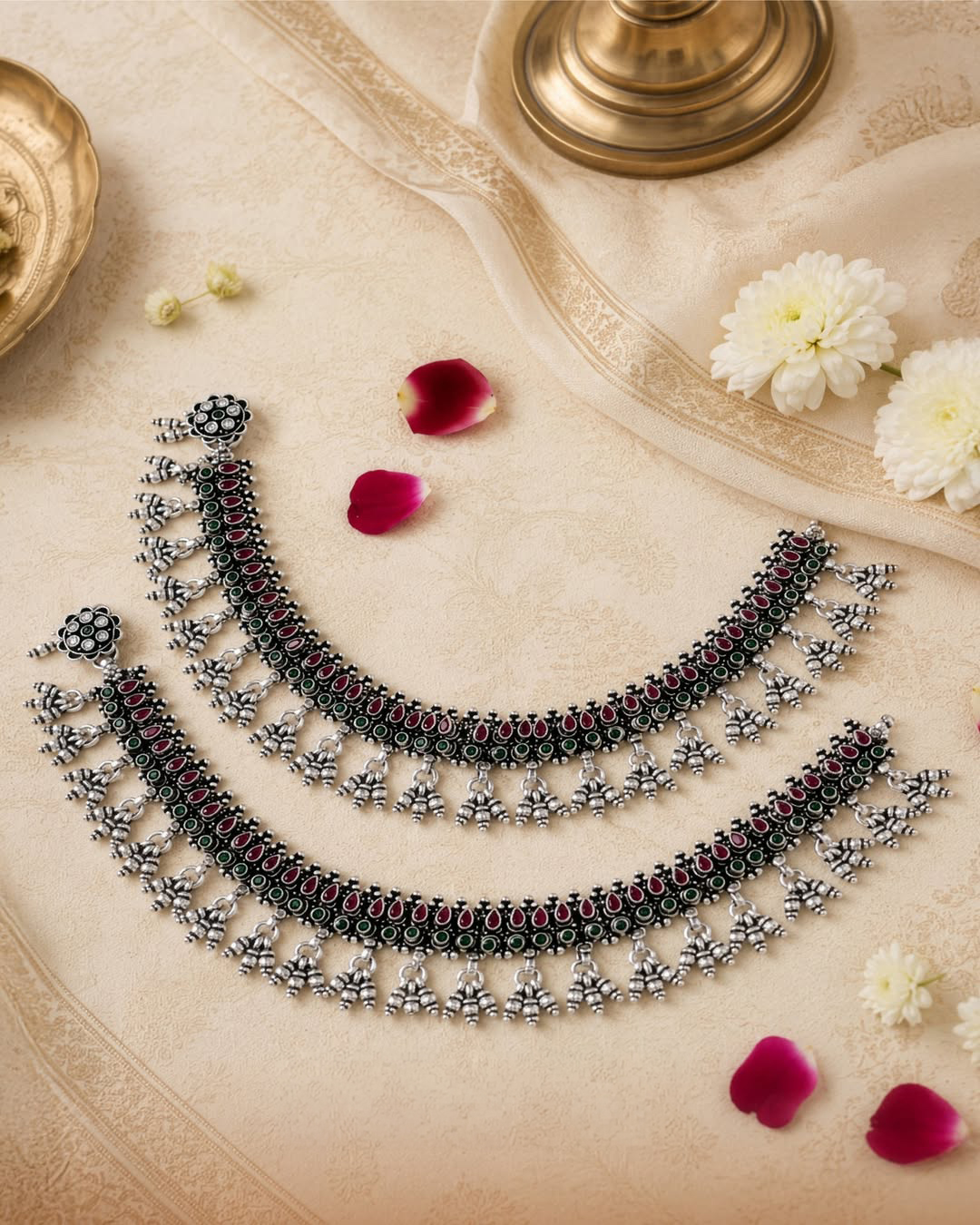 Handcrafted silver payal by Navrattan Jewellers featuring ruby and emerald-toned accents, intricate silver detailing, and traditional ghungroo drops.