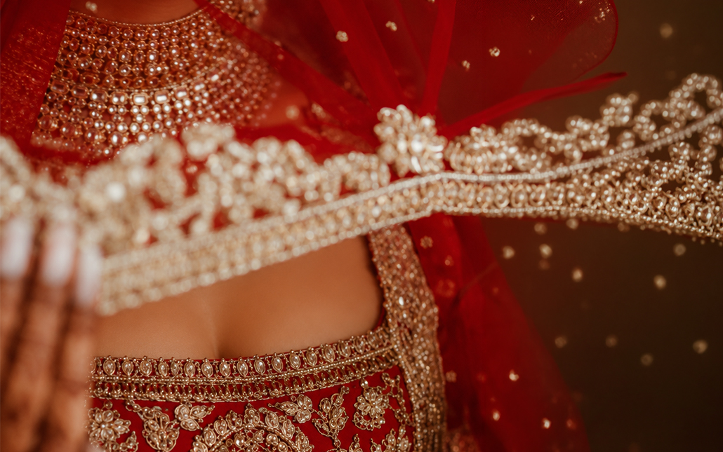 Bride in red bridal attire showcasing intricate stone-studded jewellery and an elaborately embroidered bridal lehenga.
