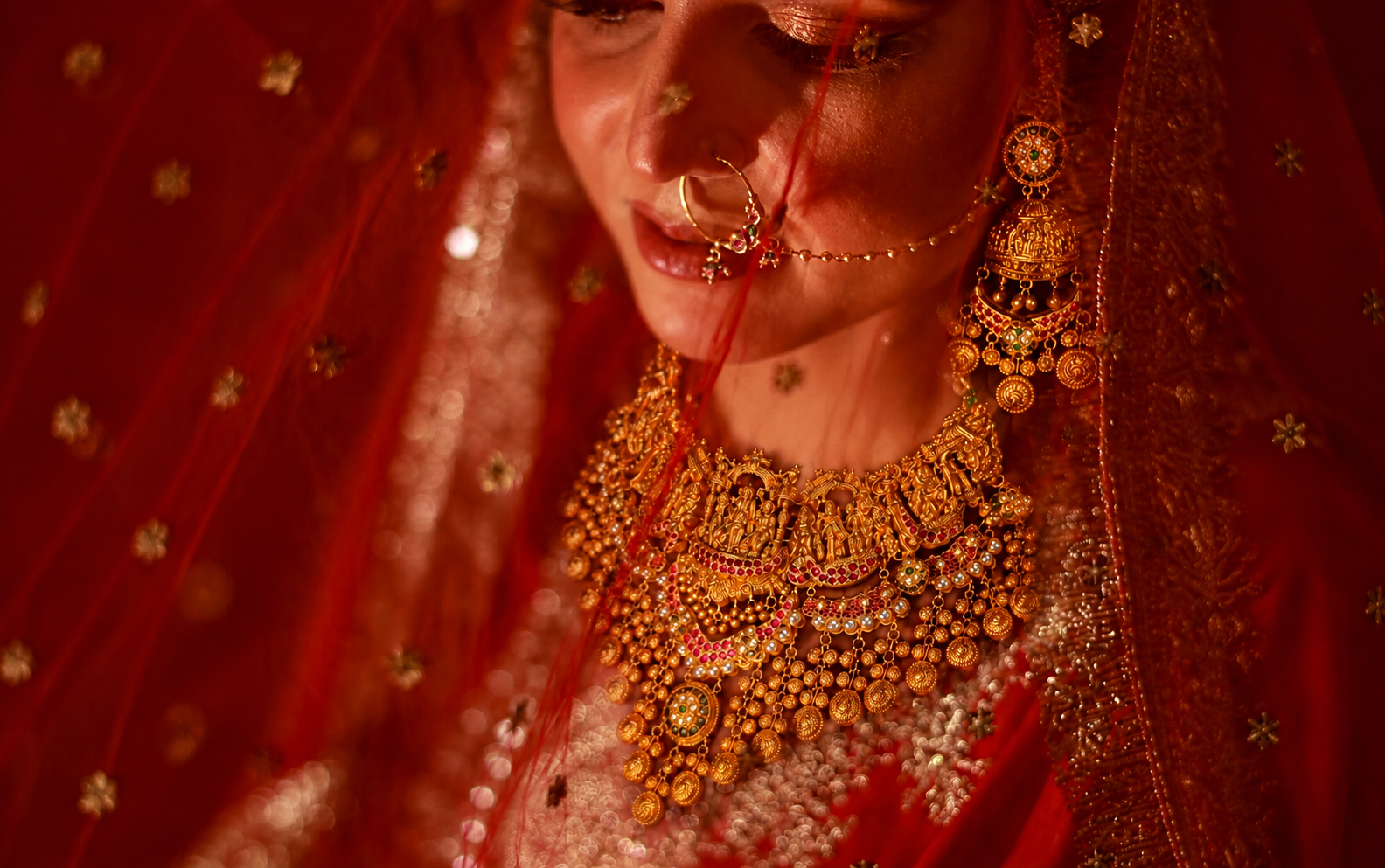 Bride in a red bridal ensemble wearing an elaborate traditional gold necklace, matching earrings and a statement bridal nath.