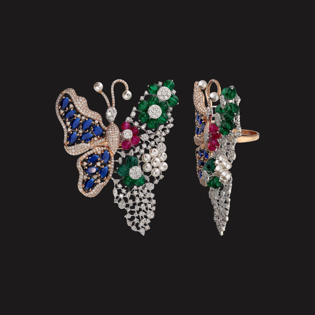 Papillon Jardin ring by Kashi Jewellers featuring blue butterflies, emerald green leaves, red gemstones and white stone detailing.