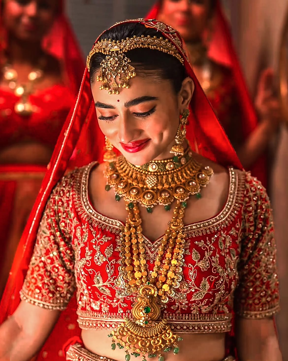 Bride wearing traditional gold bridal jewellery by Sawansukha Jewellers with layered gold necklaces, choker and emerald accents.