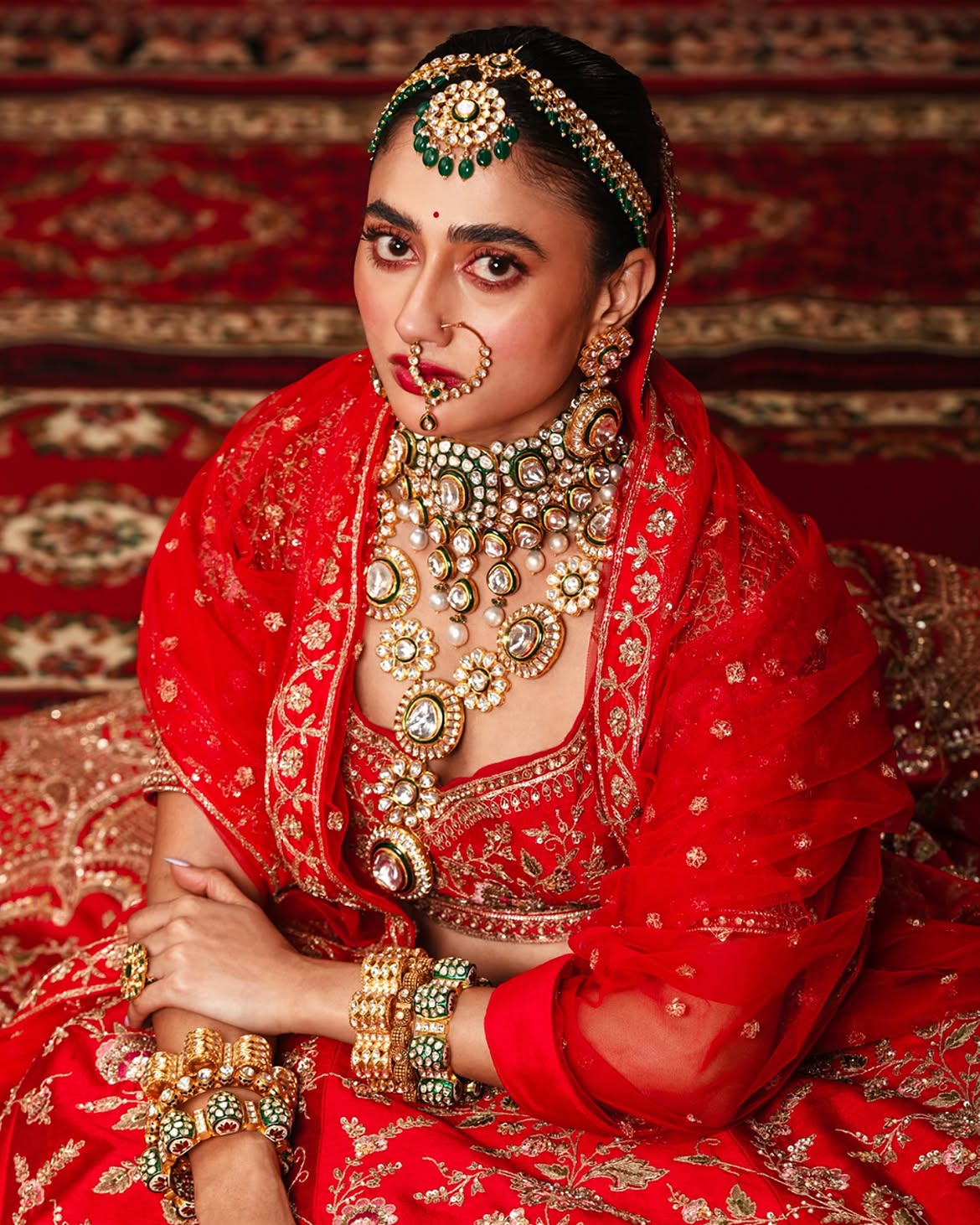 Bride wearing layered Polki, pearl and emerald bridal jewellery set by Sawansukha Jewellers with statement choker, necklaces and bridal nath.